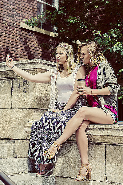 Zwei Studentinnen  die auf dem Campus zusammensitzen und ein Selbstporträt mit ihrem Smartphone machen und dabei einen dummen Schmollmund ziehen  Edmonton  Alberta  Kanada