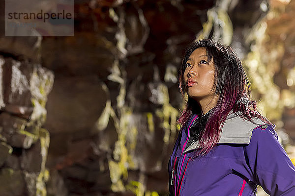 Nahaufnahme einer asiatischen Wanderin im Seitenprofil  die in einer Lavaröhrenhöhle in Island an den Höhlenwänden nach oben schaut