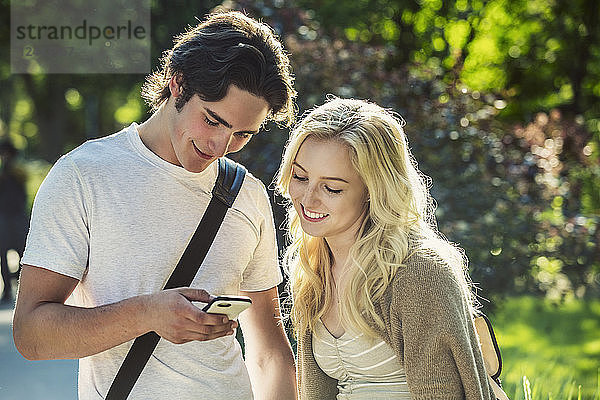 Ein junges Paar steht zusammen auf dem Universitätscampus und schaut auf ein Smartphone  Edmonton  Alberta  Kanada