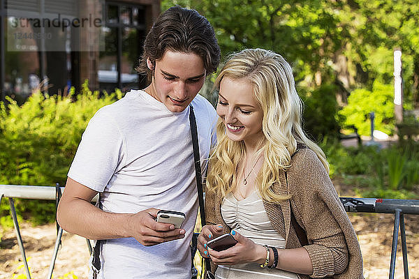 Ein junges Paar steht auf dem Universitätscampus zusammen und schaut auf ihre Smartphones  um sich gegenseitig Social-Media-Posts zu zeigen  Edmonton  Alberta  Kanada