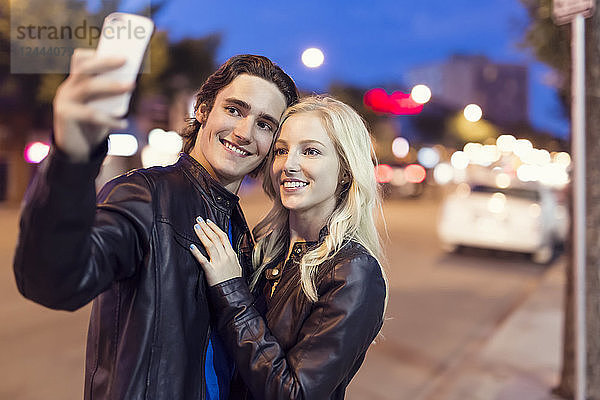 Ein junges Paar macht ein Selbstporträt mit einem Smartphone entlang einer Straße in der Abenddämmerung  Edmonton  Alberta  Kanada
