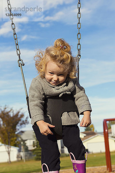 Ein niedliches junges Mädchen  das mit einem lustigen Gesicht nach unten schaut  während es auf einem Spielplatz während der Herbstsaison schaukelt  Spruce Grove  Alberta  Kanada