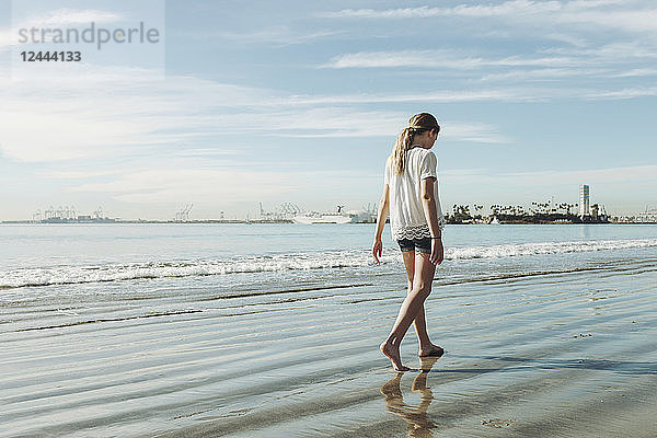 Ein Mädchen spaziert am Strand auf dem nassen Sand; Long Beach  Kalifornien  Vereinigte Staaten von Amerika
