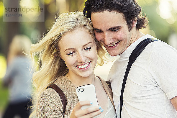Ein junges Paar  das zusammen steht und soziale Medien auf einem Smartphone abruft  während es durch einen Universitätscampus geht  Edmonton  Alberta  Kanada