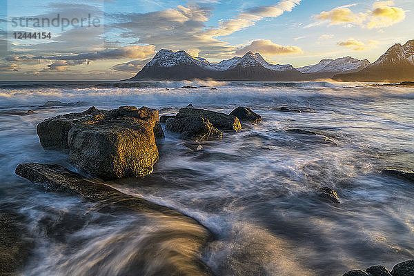 Sonnenuntergang über den Bergen der Strandir-Küste  Island  während die Brandung an die Küstenlinie schlägt  Westfjorde  Island