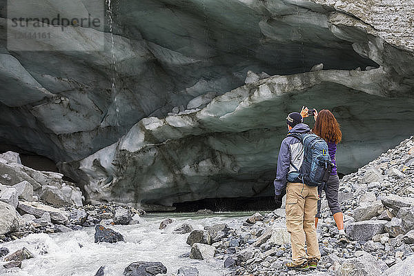 Eine Frau fotografiert mit ihrem Mobiltelefon eine Eishöhle  während sie mit ihrem Mann zum Gulkana-Gletscher wandert  Alaska  Vereinigte Staaten von Amerika