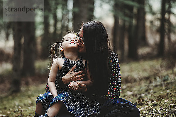 Porträt einer Mutter mit ihrer kleinen Tochter in einem Wald  das Mädchen sitzt auf dem Schoß der Mutter und schaut nach oben; Alberta  Kanada