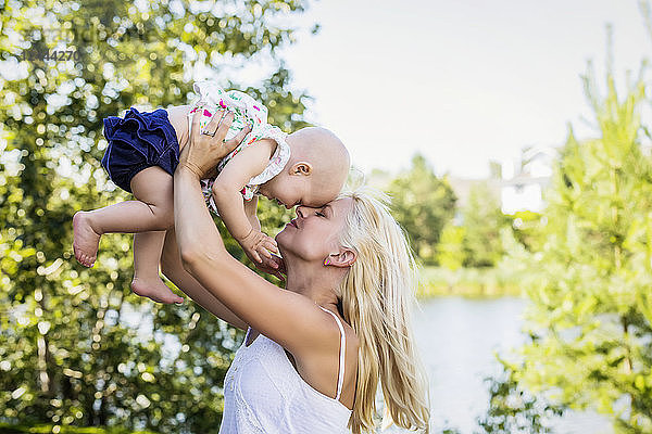 Eine schöne junge Mutter mit langen blonden Haaren genießt die Zeit mit ihrer süßen kleinen Tochter und wirft sie an einem Sommertag in einem Stadtpark in die Luft  Edmonton  Alberta  Kanada
