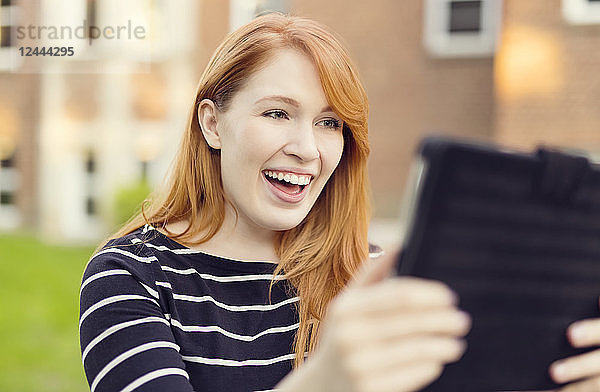 Eine junge Frau mit roten Haaren lächelt breit  während sie auf ein Tablet schaut  Edmonton  Alberta  Kanada