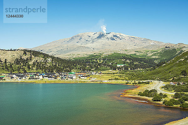 Eine kleine Stadt an einem Seeufer mit einem rauchenden Vulkan im Hintergrund; Cavahue  Neuquen  Argentinien