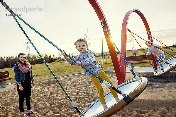 Eine junge Mutter und ihre Töchter spielen an einem warmen Herbstabend auf einer Untertassenschaukel auf einem Spielplatz; Edmonton  Alberta  Kanada