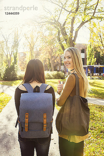 Zwei befreundete Studentinnen gehen gemeinsam über einen Universitätscampus  eine junge Frau blickt zurück in die Kamera  Edmonton  Alberta  Kanada