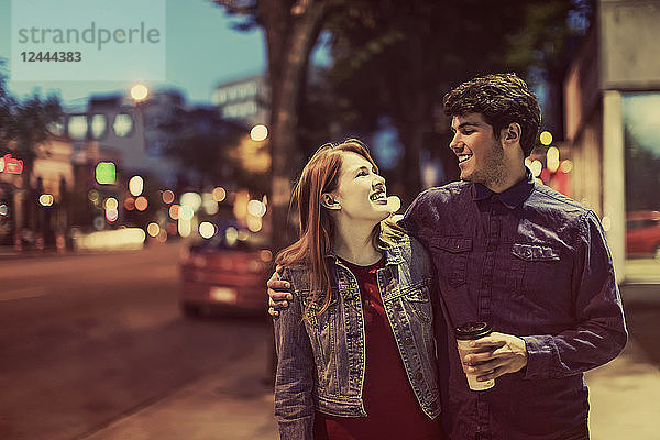 Ein junges Paar geht in der Abenddämmerung einen Bürgersteig in einem beliebten Szeneviertel entlang  Edmonton  Alberta  Kanada