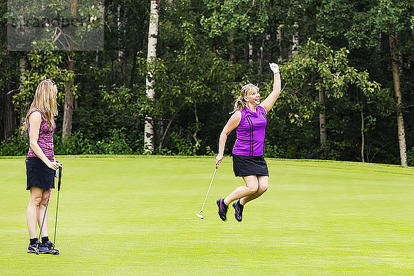 Eine reife Golferin springt vor Freude  weil sie einen Putt versenkt hat  während ihr Teamkollege zusieht; Edmonton  Alberta  Kanada