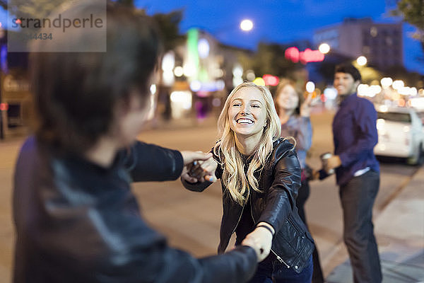 Ein junges Paar in schwarzen Lederjacken spielt nachts auf einem Bürgersteig in der Stadt  während Freunde im Hintergrund zusehen  Edmonton  Alberta  Kanada