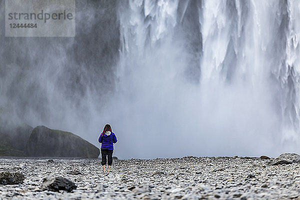 Eine Touristin blickt auf die Wasserwand des berühmten isländischen Wasserfalls Skogafoss  Island