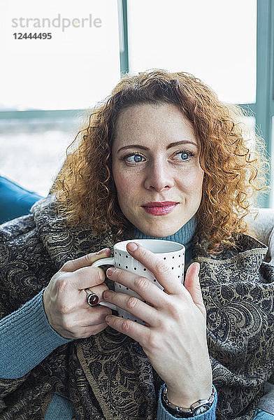 Frau mit rotem  gelocktem Haar sitzt mit einer Tasse am Fenster  Surrey  British Columbia  Kanada