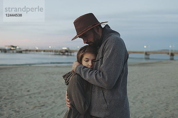 Ein Vater und seine Tochter haben einen zärtlichen Moment  der Vater hält seine Tochter in einer Umarmung an einem Strand in der Abenddämmerung; Long Beach  Kalifornien  Vereinigte Staaten von Amerika