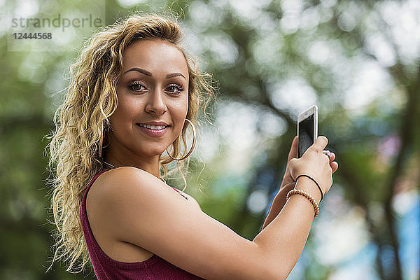 Eine schöne junge Frau hält an und posiert für die Kamera  während sie eine SMS auf ihrem Smartphone schreibt  Edmonton  Alberta  Kanada