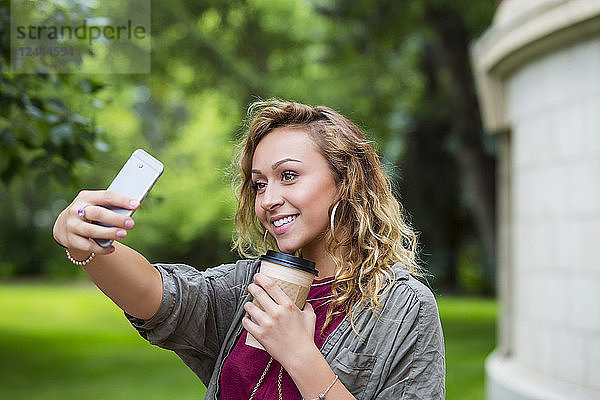 Eine hübsche Studentin macht ein Selbstporträt mit ihrem Smartphone auf dem Campus  Edmonton  Alberta  Kanada