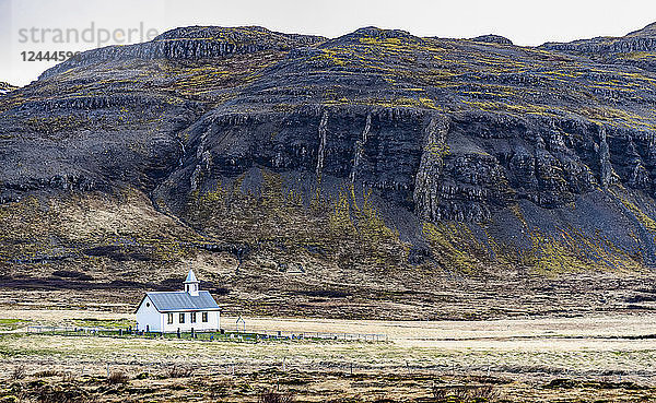 Eine Kirche und ein kleiner Friedhof werden von der umgebenden Natur in Westisland in den Schatten gestellt; Island