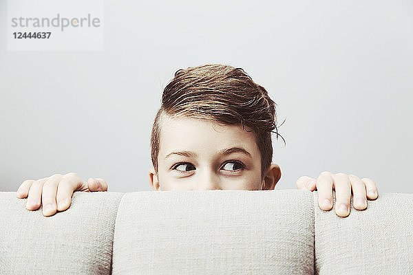 Porträt eines kleinen Jungen  der mit einem dummen Gesichtsausdruck hinter einer Couch hervorschaut; Langley  British Columbia  Kanada