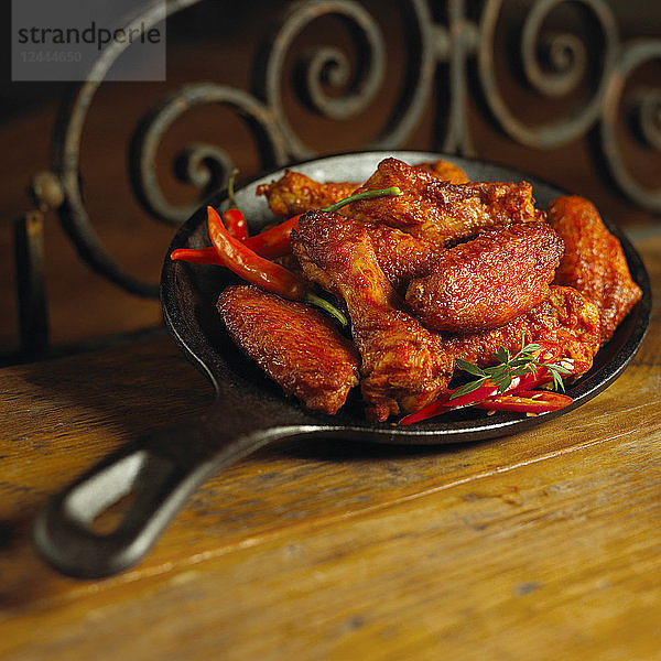 Pikante Hähnchenflügel und Paprika in einer gusseisernen Pfanne auf einem Holztisch