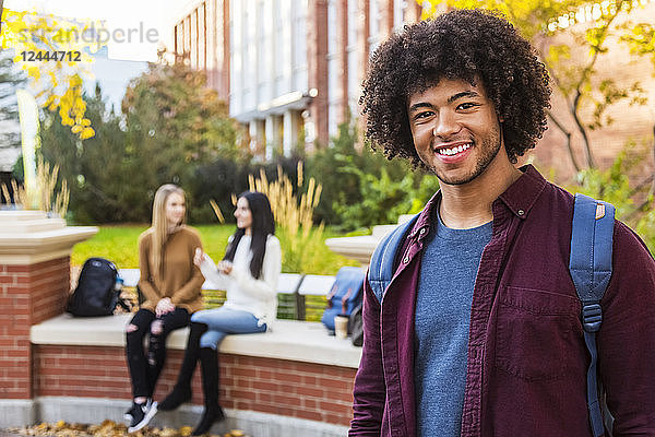 Porträt eines jungen afroamerikanischen Universitätsstudenten  der mit seinen Freunden im Hintergrund auf dem Universitätscampus posiert  Edmonton  Alberta  Kanada