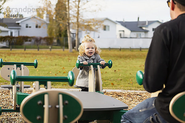 Ein süßes kleines Mädchen spielt mit ihrem Vater auf einem Spielplatz im Herbst auf einer Wippe  Spruce Grove  Alberta  Kanada