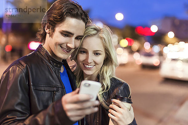 Ein junges Paar benutzt ein Smartphone auf einer Straße in der Abenddämmerung  Edmonton  Alberta  Kanada