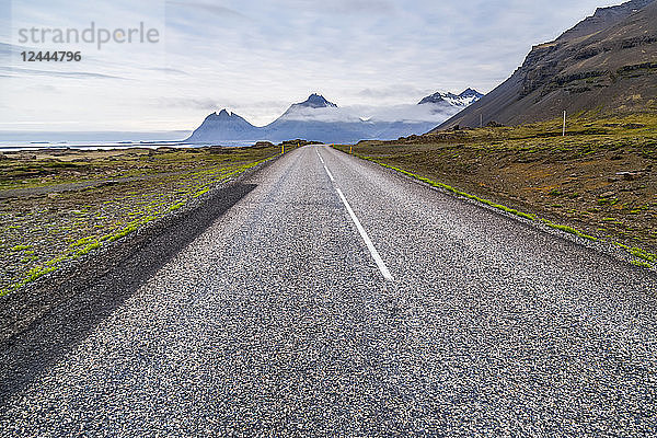 Die lange asphaltierte Straße  die in die vulkanische Berglandschaft in der Ferne führt  Island