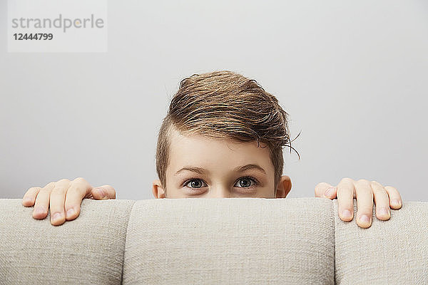 Porträt eines kleinen Jungen  der hinter einer Couch hervorschaut und in die Kamera schaut; Langley  British Columbia  Kanada