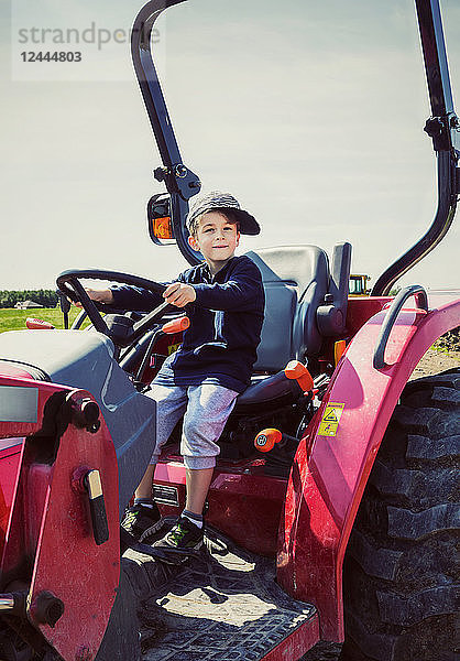 Ein kleiner Junge  der mit schief sitzendem Hut auf einem roten Traktor auf einer Farm fährt  Edmonton  Alberta  Kanada