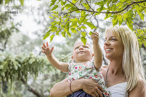 Eine schöne junge Mutter mit langen blonden Haaren genießt die Zeit mit ihrer süßen kleinen Tochter in einem Stadtpark an einem Sommertag  Edmonton  Alberta  Kanada