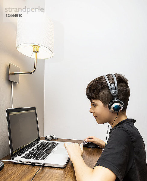 Ein kleiner Junge macht seine Hausaufgaben an einem kleinen Schreibtisch in seinem Haus und hört gleichzeitig Kopfhörer; Langley  British Columbia  Kanada