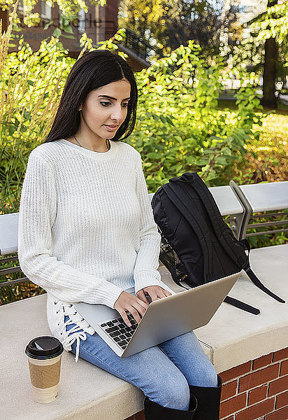 Eine junge Studentin libanesischer Abstammung sitzt auf einer Bank und benutzt ihren Laptop an einem ruhigen Ort auf dem Campus  Edmonton  Alberta  Kanada