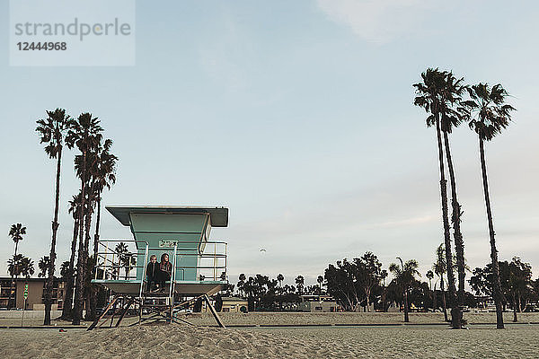 Zwei Mädchen sitzen in der Morgendämmerung auf einer Rettungsschwimmerstation und schauen auf den Ozean hinaus; Long Beach  Kalifornien  Vereinigte Staaten von Amerika