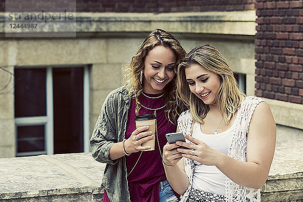 Zwei Studentinnen stehen zusammen auf dem Campus und schauen auf ein Smartphone  Edmonton  Alberta  Kanada