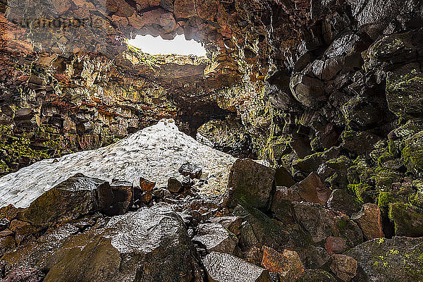Bei einer Wanderung durch die Lavaröhrenhöhlen in der Nähe von Reykjavik im Frühsommer ist der Schnee in der Höhle noch nicht ganz geschmolzen. Besucher wandern hier auf dem Pfad der Lava  die während eines Ausbruchs geflossen ist  Island
