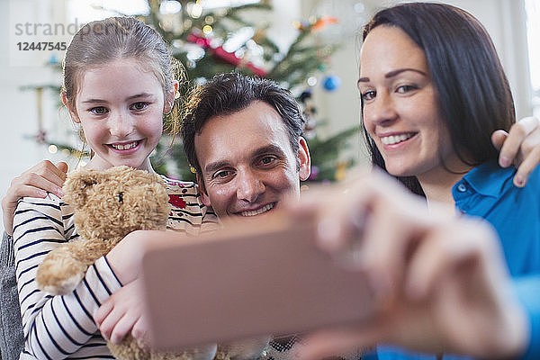 Glückliche Familie mit Smartphone  die ein Selfie im Weihnachtswohnzimmer macht