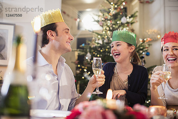 Eine glückliche Familie in Papierkronen genießt das Weihnachtsessen  trinkt Champagner und lacht