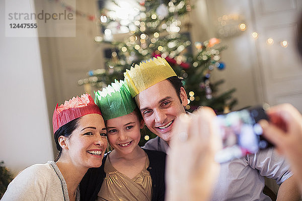 Glückliche Familie mit Papierkronen posiert für ein Foto im Weihnachtswohnzimmer