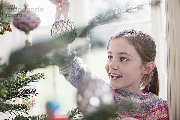 Mädchen schmückt  hängt Ornament an Weihnachtsbaum