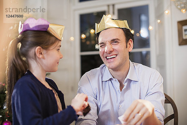 Glücklicher Vater und Tochter mit Weihnachtskronen aus Papier lachen