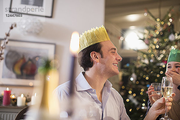 Glücklicher Vater und Tochter in Papierkronen trinken Wasser und Champagner beim Weihnachtsessen bei Kerzenschein