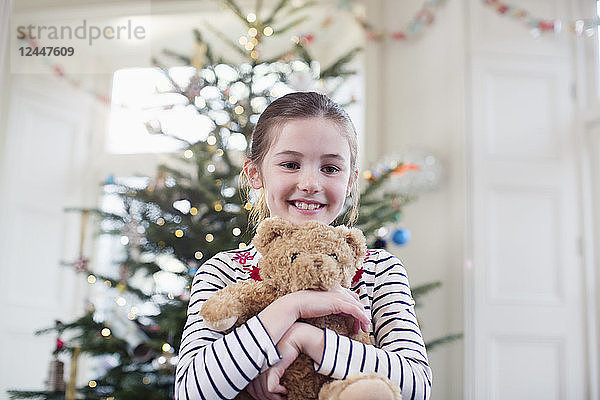 Porträt lächelnd  süßes Mädchen hält Teddybär vor Weihnachtsbaum