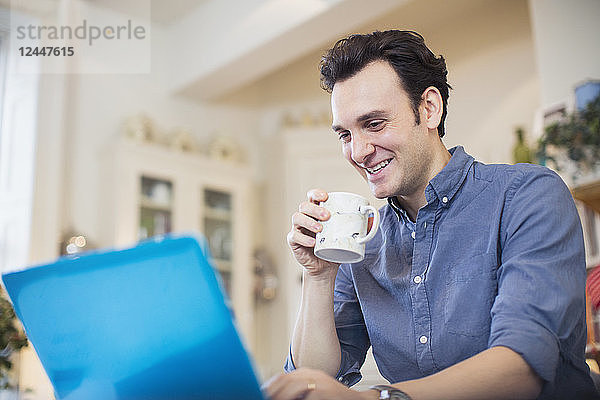 Lächelnder Mann trinkt Kaffee und arbeitet am Laptop