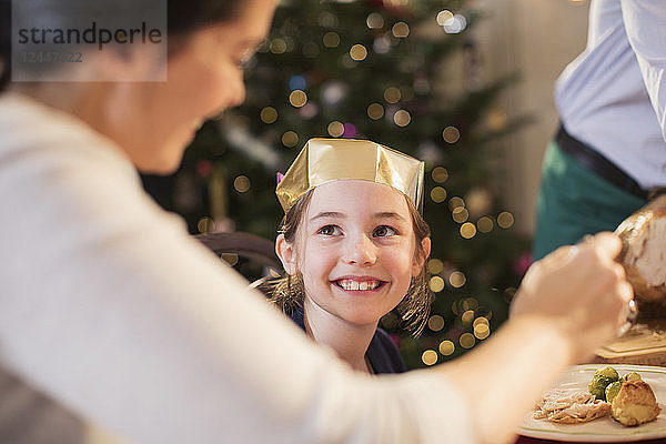 Lächelndes Mädchen mit Papierkrone genießt das Weihnachtsessen