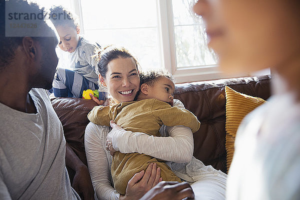 Glückliche Mutter kuschelt mit ihrem kleinen Sohn und entspannt sich mit ihrer Familie auf dem Wohnzimmersofa