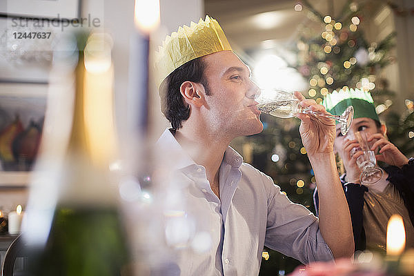 Tochter beobachtet glücklichen Vater mit Papierkrone  der beim Weihnachtsessen Champagner trinkt